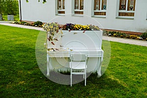 White piano and chairs with romantic decor in summer in garden. Decor for a wedding or a romantic dinner. Grand piano
