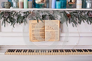 White piano with music book. Piano decorated branches of a Christmas tree, cones and a garland. Vintage old classic piano with mus