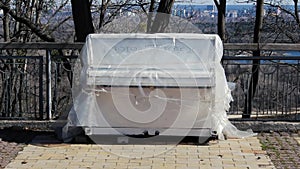 A white piano stands in the street. Tool under the plastic film