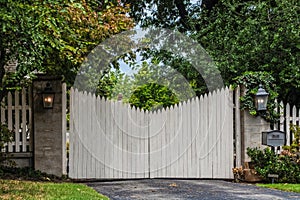 White picket electric gate entrance to estate with mailbox and packages hidden behind bushes and no soliciting sign on leafy