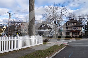 White picket fence street and sidewalk of suburban homes with leafless late fall winter season trees