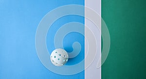 White pickleball ball on blue and green playing surface