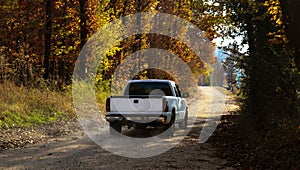 White pickup truck driving down dusty dirt road with fall leaves and dust behind