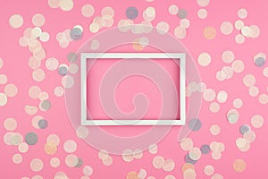 White picture frame and confetti on pink background.