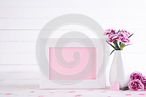 White picture frame with lovely pink carnation flower in vase on white wooden table