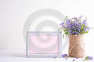 White picture frame with lovely purple flower in vase on white wooden table