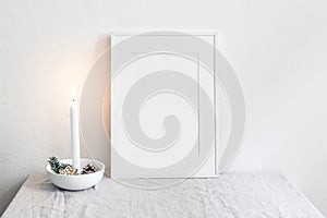 White picture frame mockup scene. Christmas seasonal still life. Burning candle in ceramic candle holder. Scandinavian