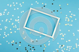 White picture frame and sequins stars on blue background.