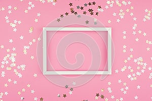 White picture frame and sequins stars on pink background.