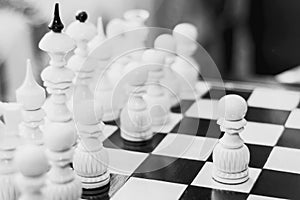 The white piece is a pawn on a wooden chessboard. Black and white photo of chess.