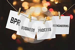 White pieces of paper with the text BPR Business process reengineering hang on a rope against a multicolored bokeh background