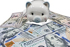 A white piggy bank against a white background watches over a pile of United States currency. Wealth, Savings, inflation concept -