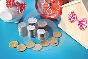 White piggy bank and alarm clock with wood house on table