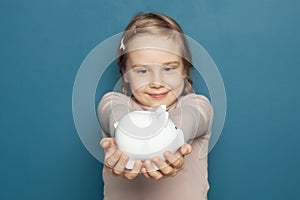 White piggy bank in hand of happy child girl on blue background. Focus on money bank