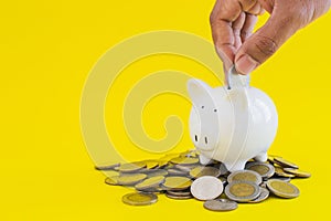 White piggy with coins thai baht and hand putting money on yellow background.