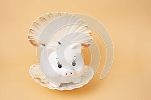 White piggybank in a oyster sea shell on very soft orange background
