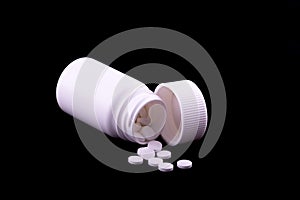 A white pill bottle with white pills on an black background