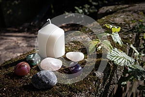 White Pillar candle with small collection of crystal tumbled gem stones in rustic setting