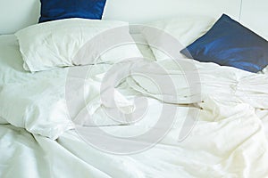 White pillow and dark blue on bed and with wrinkle messy blanket in bedroom, from sleeping in a long night, an unmade bed in hotel