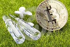 White pills and ampules with bitcoin coin on the grass background - healthcare cost concept