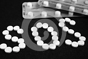 White pills on black background, which forming the word SOS, with a blister of pills on background.