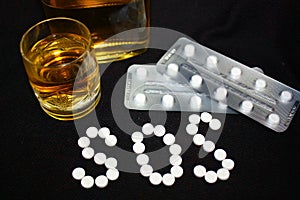 White pills on black background, which forming the word SOS, with glass and bottle of alcohol.