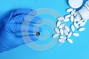 White pills and a black pill in hand with blue glove. Different pills. Medical and different concept of light blue paper