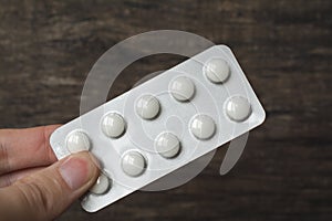 White pills blister hand holding over wood background, painkiller, sedative, antibiotic or drug medicine concept