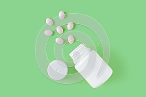 White pills and bottle on green background.
