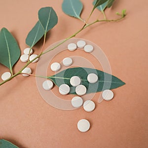 White pills on a brown background with a green plant. Medicine, health, beauty.