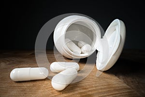 White pills or capsules next to bottle on wooden table background. Drug prescription, treatment medication. Pharmaceutical