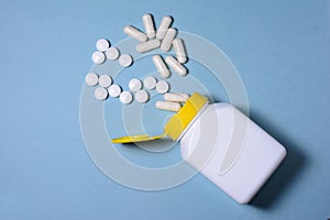 White pills and capsules poured from a plastic medical jar on a blue background