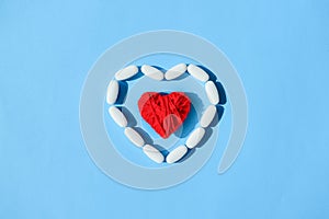 White pills capsules and red thread heart shape on blue backgrou