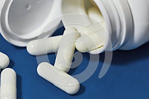 White pills, capsules scattered from a white bottle, jar on a blue background