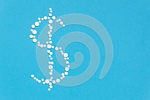 White pills in dollar sign shape on blue background. Pharmaceutical concept of medical expenses and prices for medicine