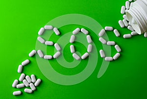 White pills on green background, which forming the word - SOS, with a blister of pills on background.