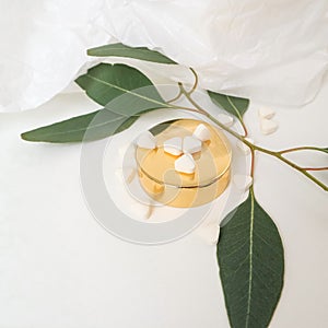 White pills with green leaves on a white background with a golden lid from a jar. Medicine, beauty, health. Space for