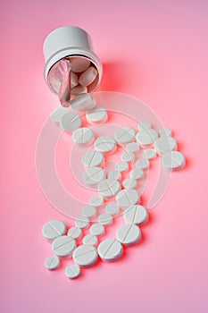 White pills are laid in the dollar sign on a pink background.White pills fell out of a still bottle