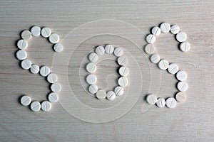 White pills laid out in a word SOS on a table