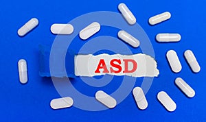 White pills lie on a beautiful blue background. In the center is white paper with the inscription ASD Autism Spectrum Disorder.