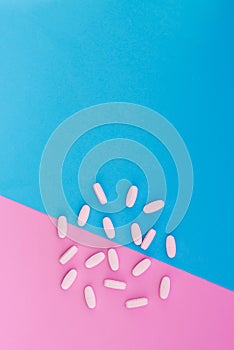 White pills lie on a colored background. Vitamins on blue and pink pastel background. Place for text. Top view