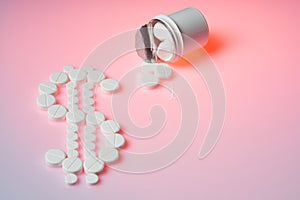 White pills lie in the shape of a dollar on a pink background. Bottle with medicines lies on a pink background