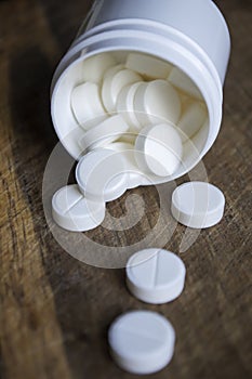 White pills poured out of the box onto a wooden table. White pills. Medical tablets in white plastic packaging.