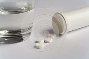 White pills and pill bottle with glass of water on white background medicine pharmacy health
