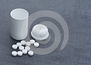 White Pills scattered across a Gray Background and an Open Bottle. Top View Closeup.