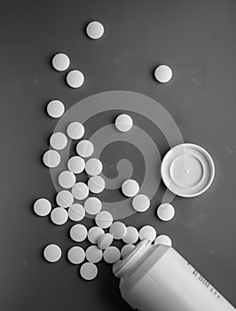 White pills scattered from a white jar on a black and whait background