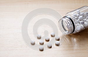 White pills are scattered on a wooden table.  Empty space on the left.