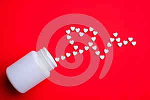 White pills in the shape of cardiography near white plastic bottle on red table