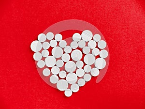 White medicine pills in the shape of a heart on a red background top view with copy space.