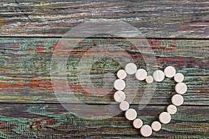 White pills in the shape of a heart on a wooden background